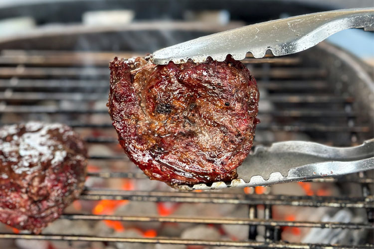 a cooked ribeye cap being held by tongs over charcoal