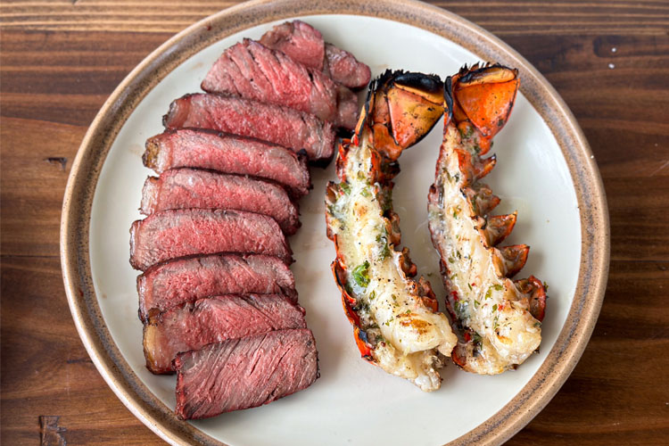 sliced ny strip and lobster tails on a plate