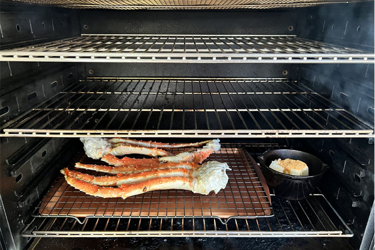 crab legs in the smoker with a pot of butter sauce beside them