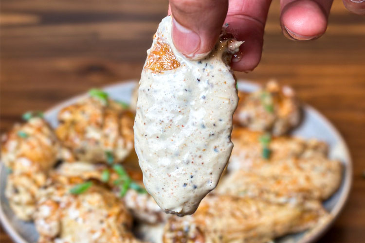 fingers holding a wing covered in alabama white sauce