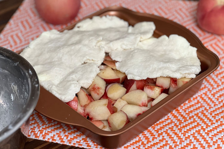 raw peach cobbler being covered with dough