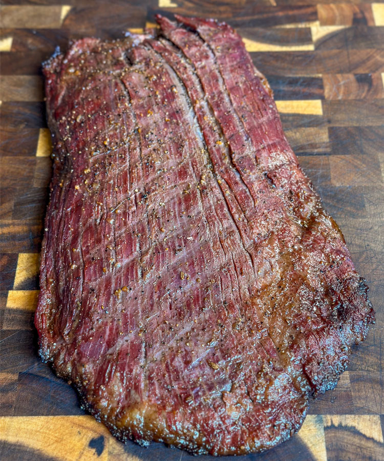 cooked flank steak on a wooden chopping board