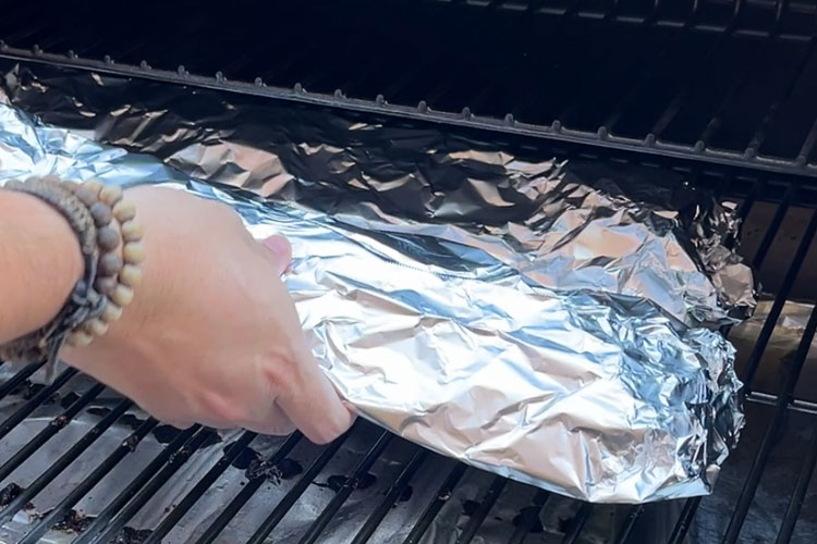 foil wrapped ribs being placed in the smoker