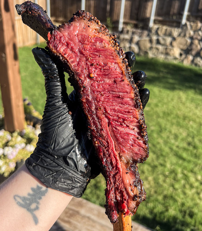 a single pastrami dino rib being held by a black gloved hand