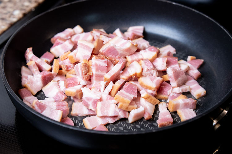 raw cubed bacon in a frypan