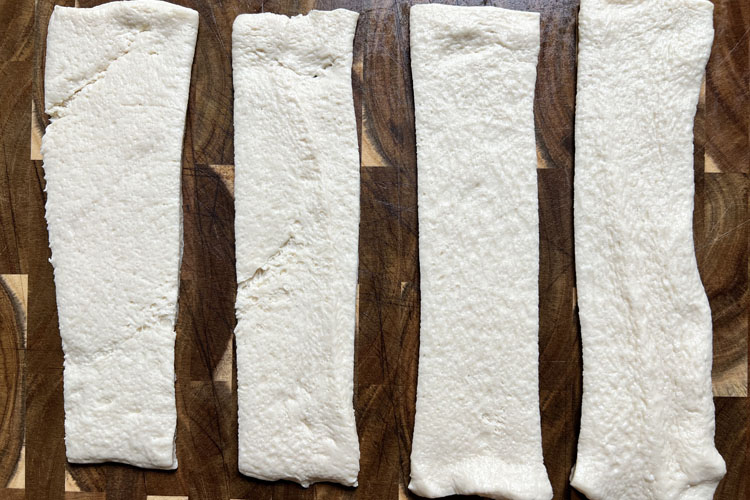 uncooked stips of pizza dough on a wooden board