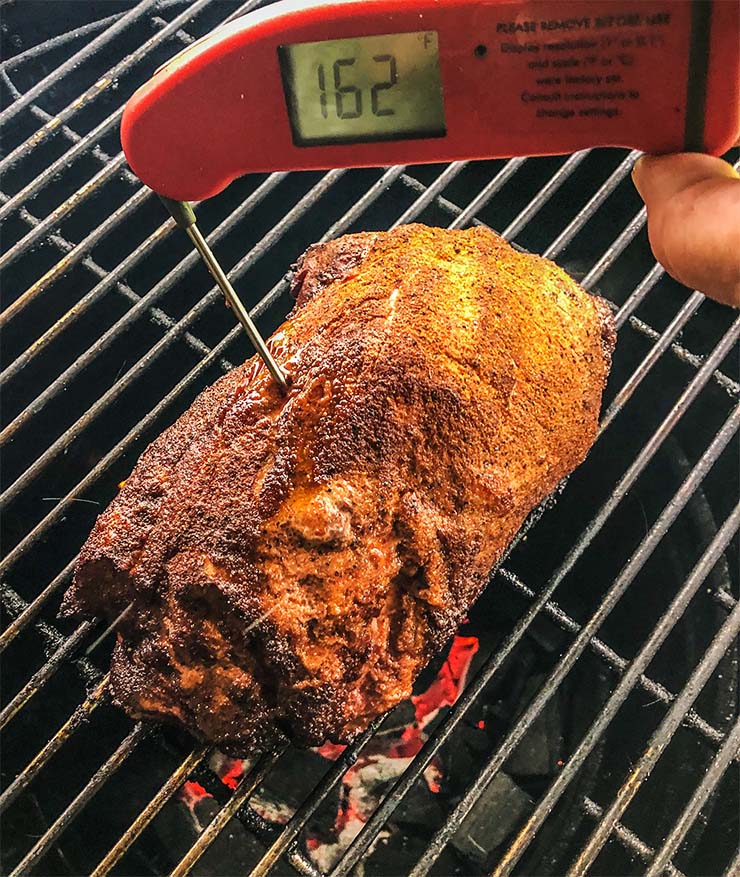 instant read thermometer inserted into a piece of pork butt on the smoker