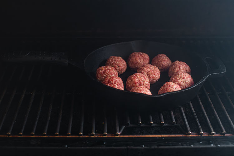 raw meatballs in a cast iron pan in the smoker
