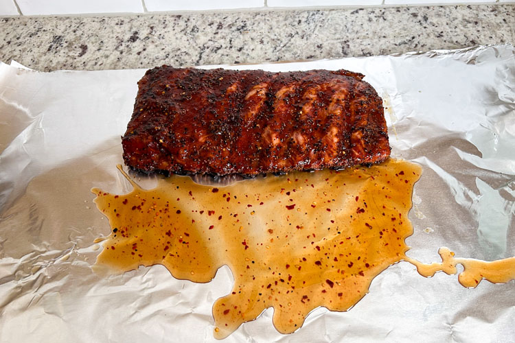 western carolina ribs sitting on foil with mop sauce on it