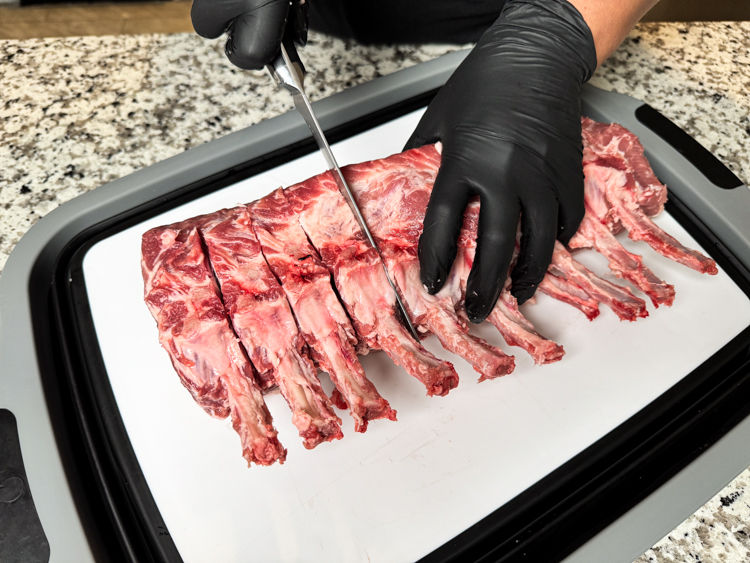 a black gloved hand slicing a pork rack