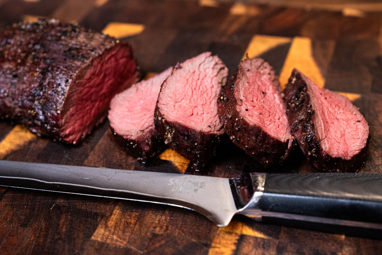 sliced teres major steak on a wooden chopping board