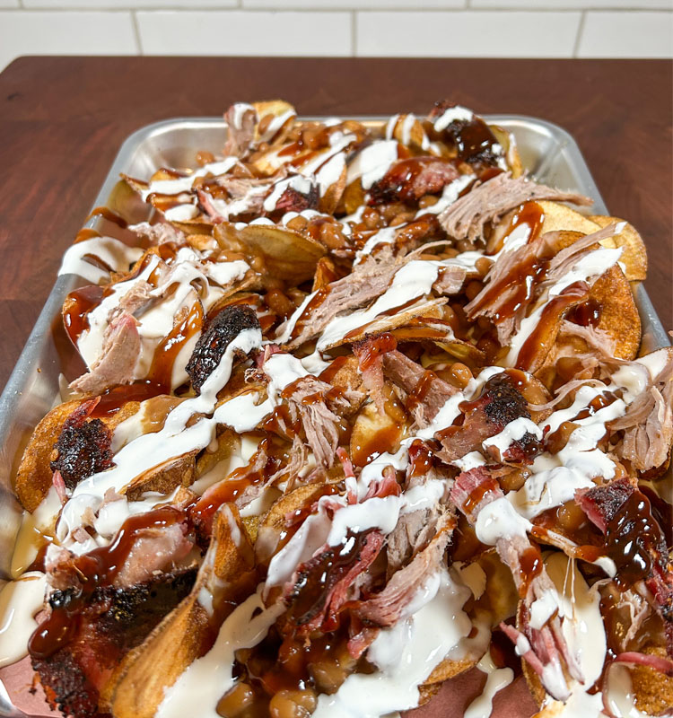 chips on a metal tray with queso, baked beans, pulled pork