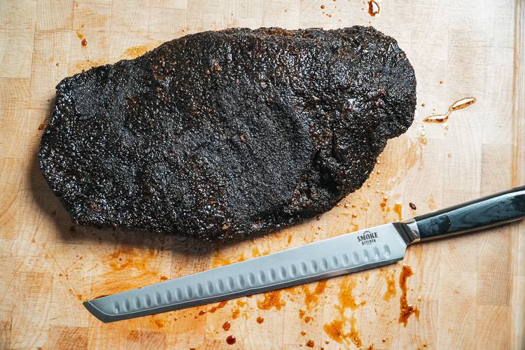 smoked costco brisket with smoke kitchen knife on a wooden chopping board