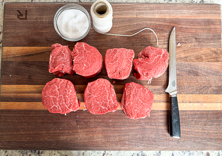 filets on a wooden chopping board with a boning knife, string and a bowl of salt