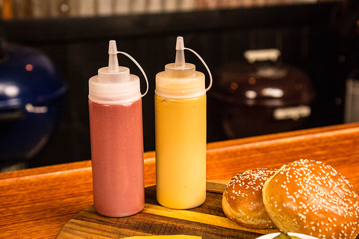 two squeeze bottles filled with bbq sauce on a wooden table