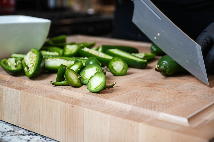 jalapenos on a wooden chopping board with ends being cut off