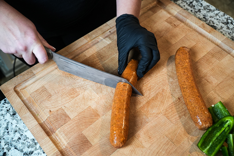 a whole smoked pork sausage being cut on a wooden chopping board