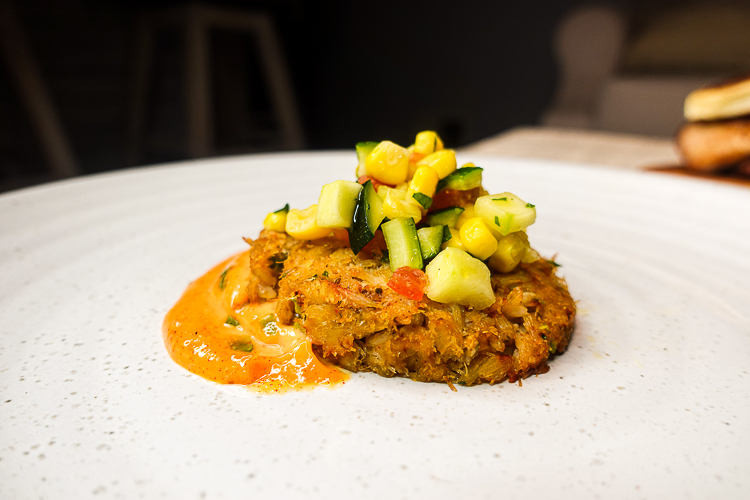 crab cake plated on white plate with succotash and remoulade