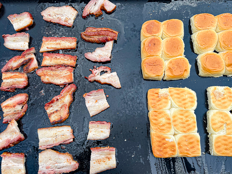 pork belly searing and slider buns toasting on a griddle