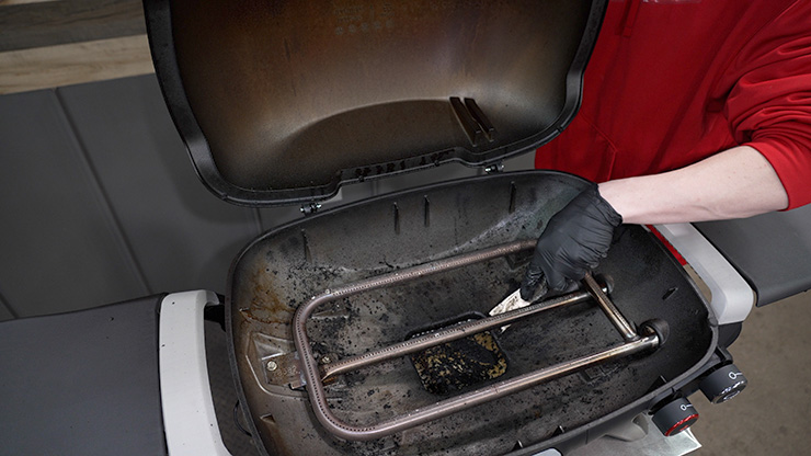 a person cleaning inside the Weber Q+ grill chamber