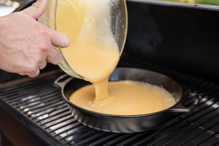 pouring cornbread mixture into hot skillet on the smoker