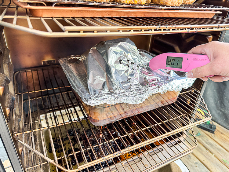 taking the temperature of the foil covered smoked ham in the smoker