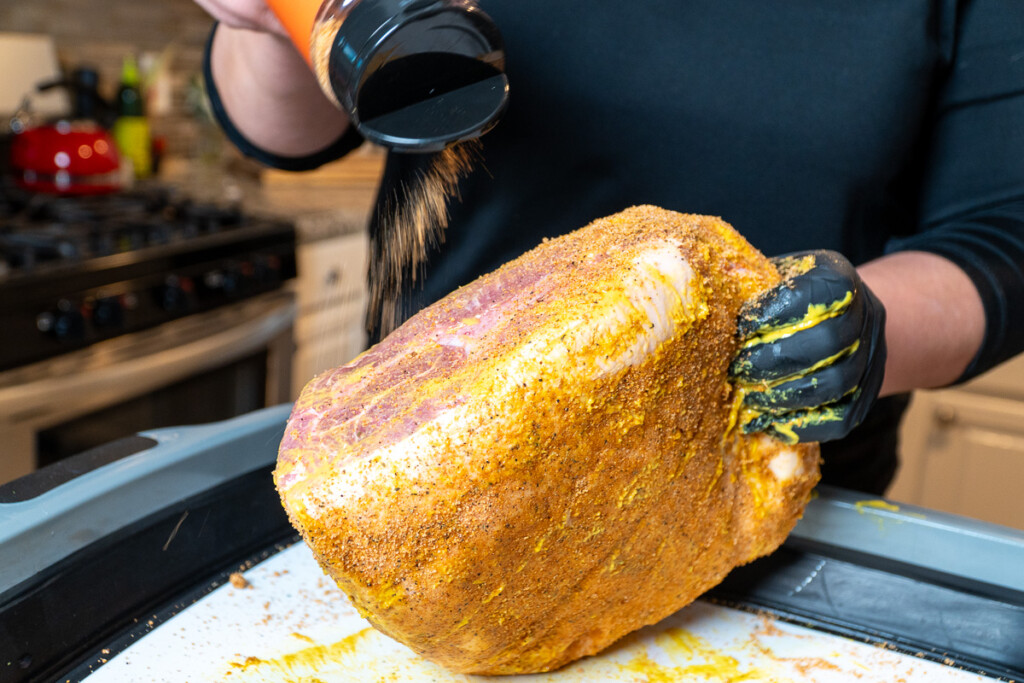 a pork butt being held on its edge and being sprinkled with bbq rub