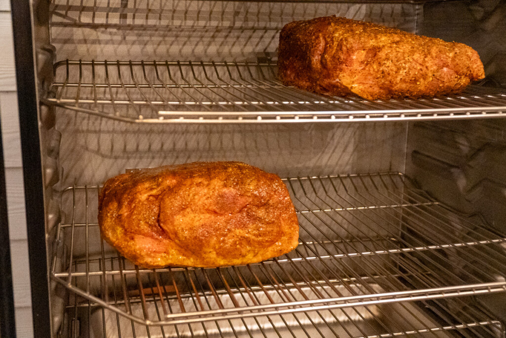 two raw pork butts on shelves in a smoker