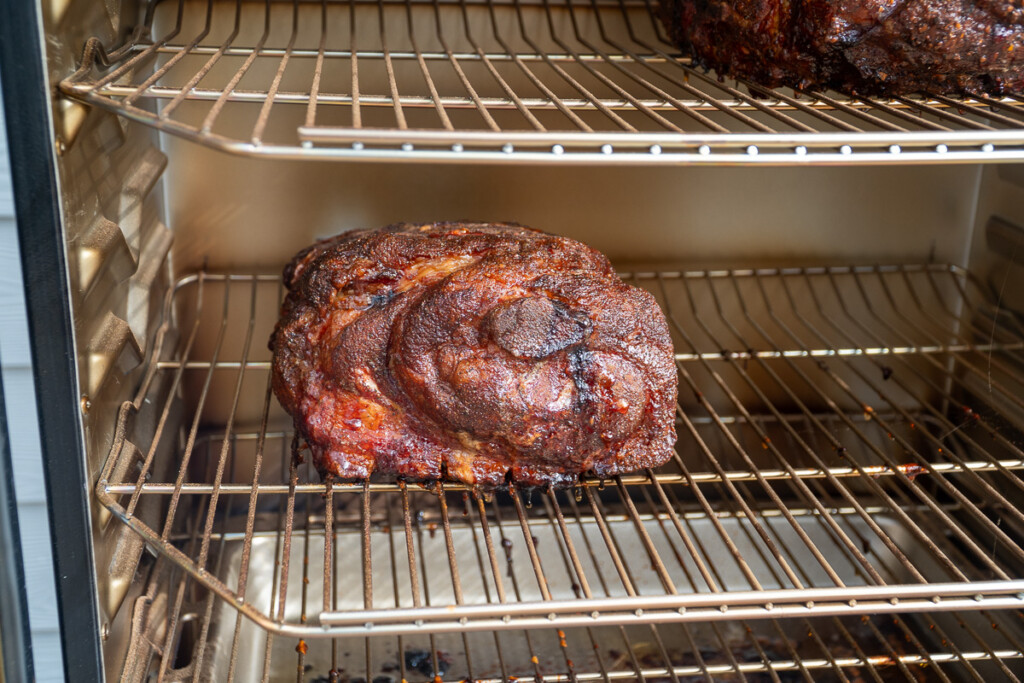 a cooked pork butt on a shelf in the smoker before wrapping