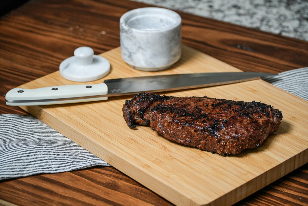 steak resting on a wooden board with a knife beside it