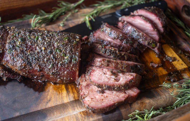 Sliced smoked beef tenderloin with a flavorful herb and spice crust served on a wooden cutting board garnished with fresh rosemary.