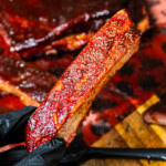 Smoked 3-2-1 pork ribs with glossy bark, held close to camera to show tender meat and caramelized surface