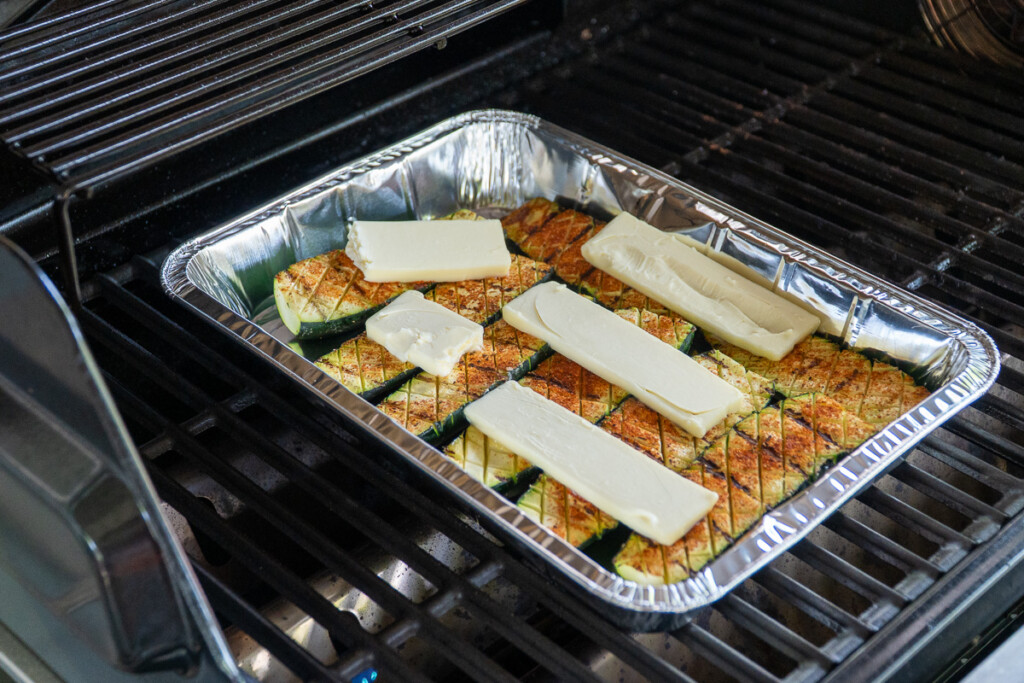 zucchini in an aluminum pan with pats of butter on the top, in the grill