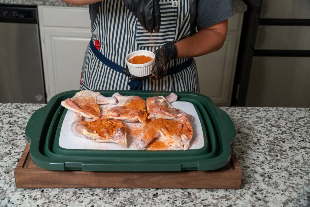 a person sprinkling seasoning on raw chicken quarters